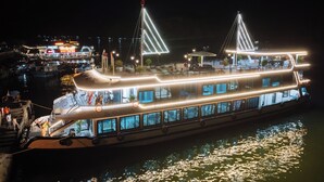 Een grote, verlichte boot met meerdere dekken, met een opvallende brugconstructie en een eetgedeelte met terras.