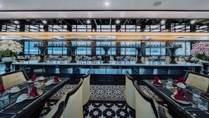 Een restaurant met meerdere eettafels, vloeren met een zwart-wit patroon en grote ramen met uitzicht op zee.