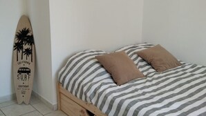 A single bed with striped bedding and two pillows, a wooden floor, and a surfboard leaning against the wall. - Family-Friendly 4-Bedroom House with Garden – Arcachon Bay, Gujan-Mestras (Gujean-mestras)