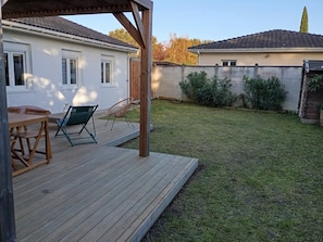 Une terrasse en bois avec des meubles d’extérieur, un patio couvert et une pelouse bien entretenue.