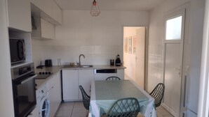 A compact kitchen with a microwave, oven, washing machine, sink, and a dining table with chairs. - Family-Friendly 4-Bedroom House with Garden – Arcachon Bay, Gujan-Mestras (Gujean-mestras)