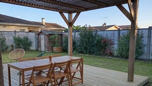 A wooden deck with a table and chairs, surrounded by a garden and a fence. - Family-Friendly 4-Bedroom House with Garden – Arcachon Bay, Gujan-Mestras (Gujean-mestras)
