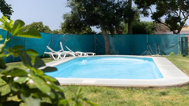Ein rechteckiger Swimmingpool mit weißem Rand, umgeben von einem grünen Zaun und weißen Liegestühlen.