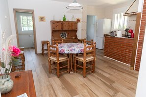 Un comedor con una mesa redonda de madera, sillas, un armario y una zona de cocina con pared de ladrillo y un refrigerador.