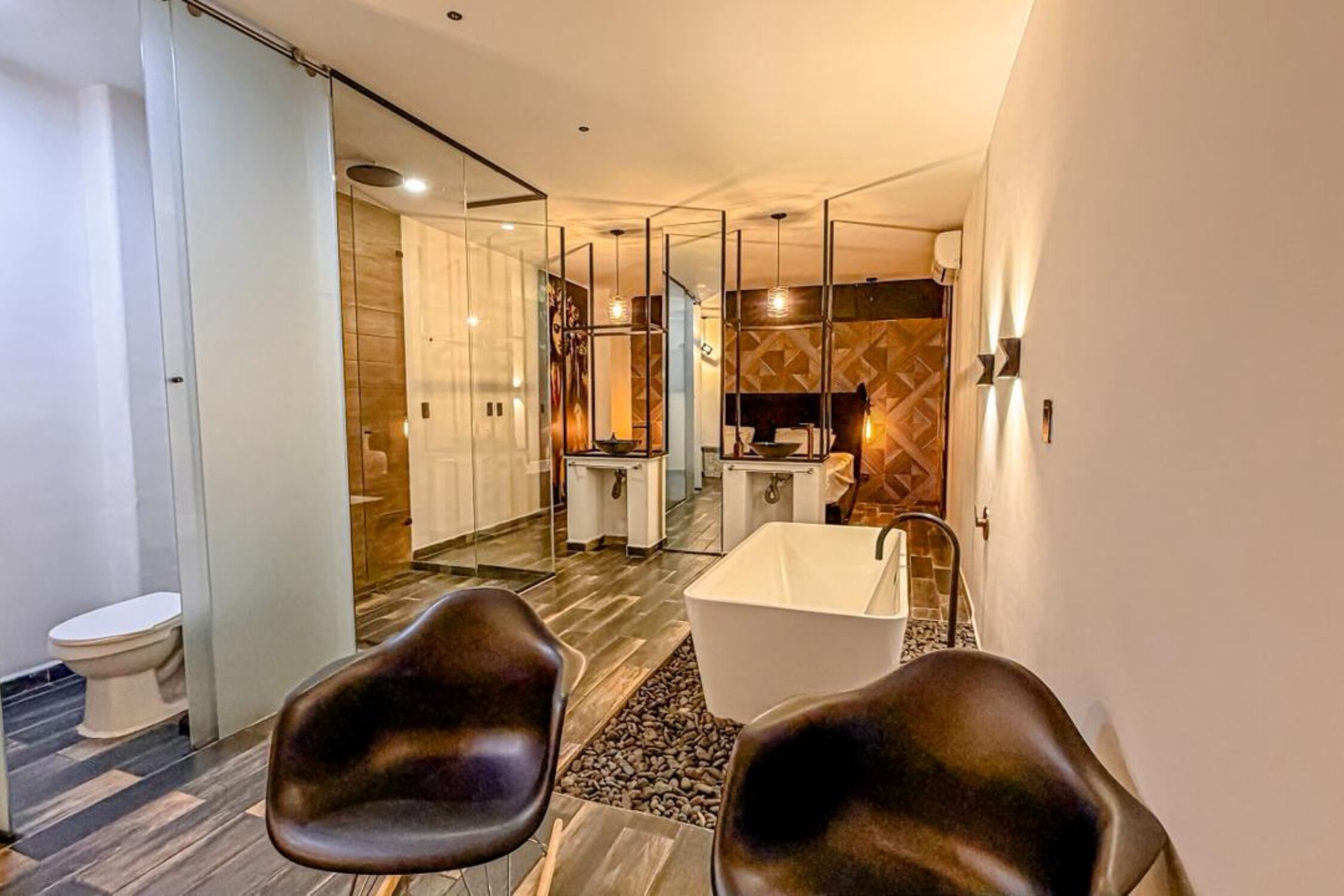 A modern bathroom with a glass partition, a bathtub, a toilet, and two chairs.