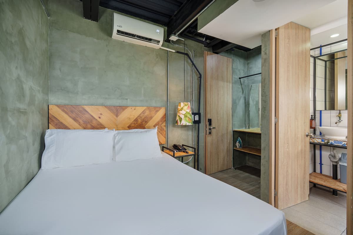 A hotel room with a bed, a wooden headboard, a small bedside table with a phone, and a shower area with a glass door.