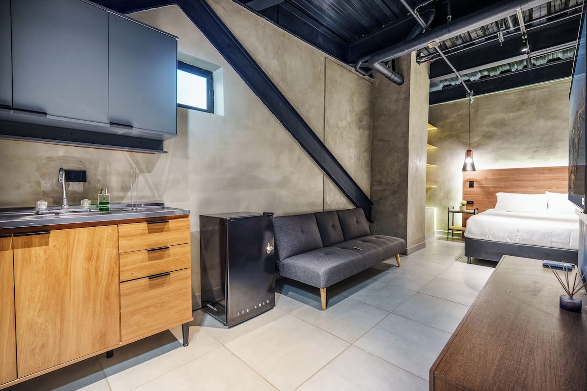 A modern kitchen with wooden cabinets, a built-in oven, and a grey sofa in a combined living and dining area.
