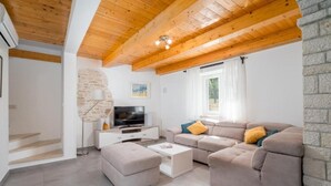 Ein modernes Wohnzimmer mit Holzbalkendecke, Steinwand, einer Sofagarnitur, einem Fernseher und einer Treppe.