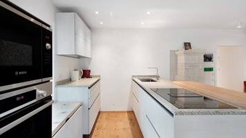 A modern kitchen with a Bosch microwave, white cabinets, a wooden floor, and a built-in sink.