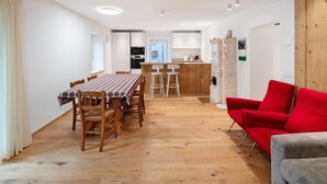 Ein Essbereich mit Holztisch und -stühlen, einem roten Sessel und einer Küche im Hintergrund.
