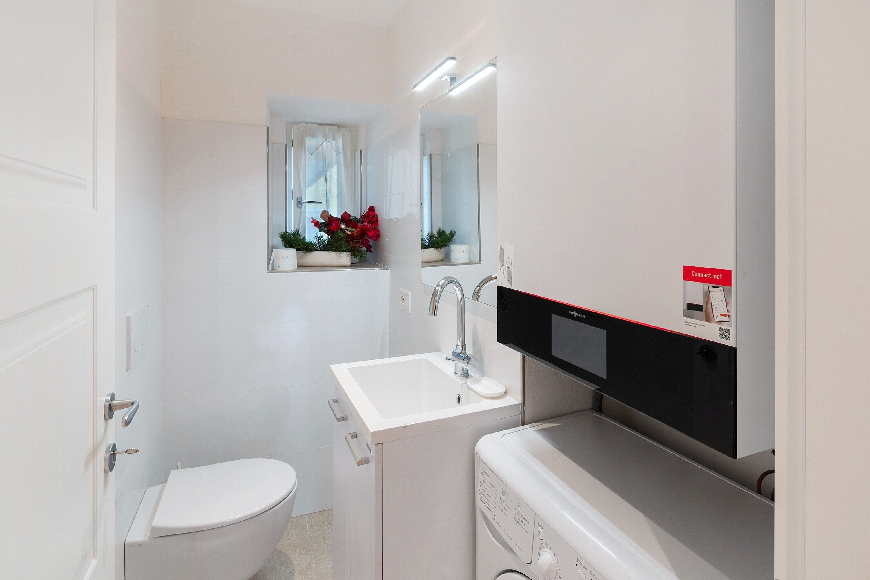 Une salle de bain équipée de toilettes, d’un lavabo, d’un miroir et d’un lave-linge.