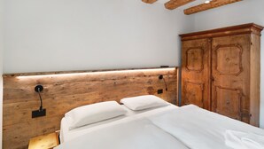 Ein Schlafzimmer mit Holzkopfteil, einem Bett mit weißer Bettwäsche, einem Nachttisch mit Lampe und einem hölzernen Kleiderschrank.