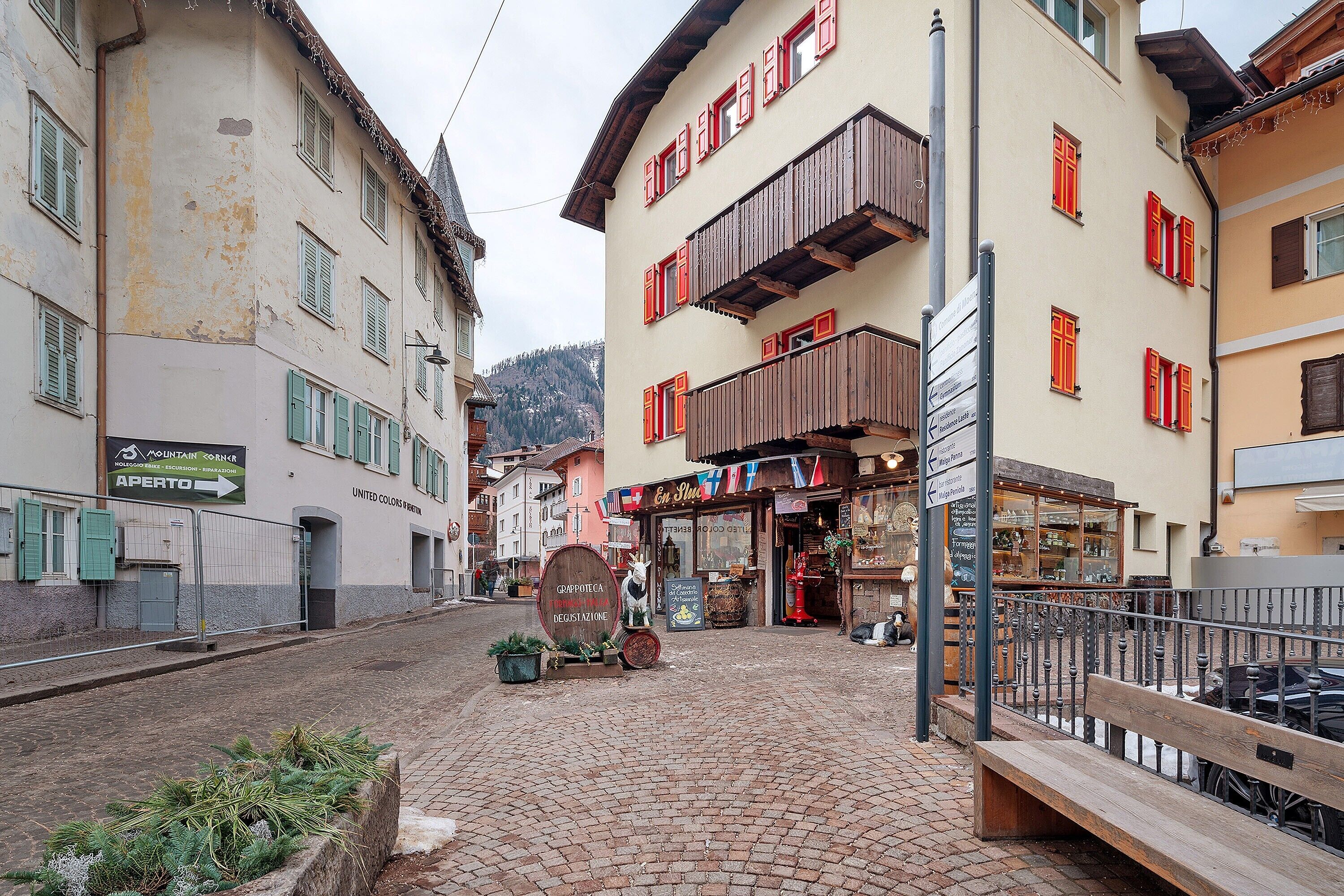 Une rue pavée bordée d’immeubles, avec un banc et une enseigne indiquant un restaurant.