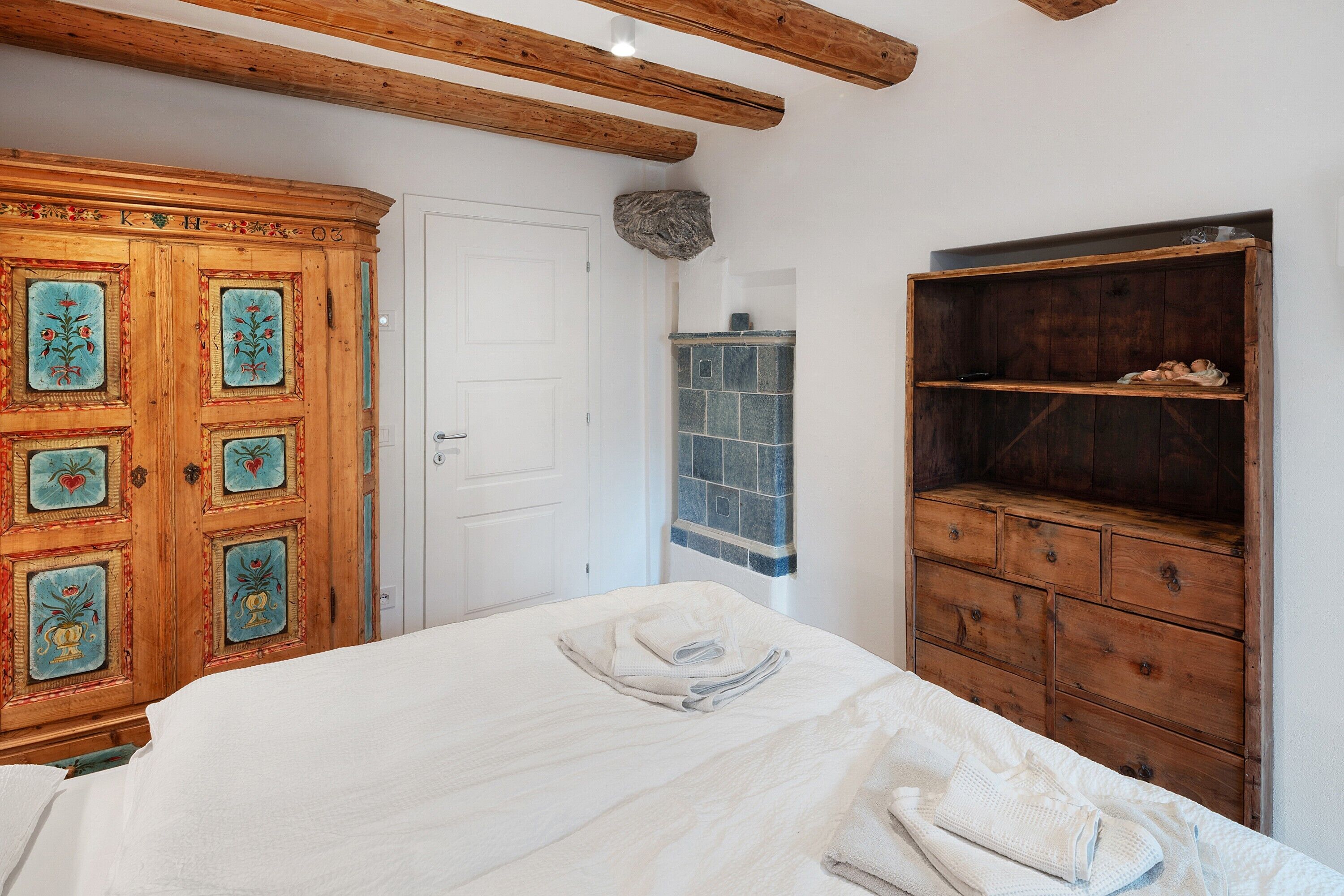 A bedroom with a bed, wooden wardrobe, and a tiled fireplace.