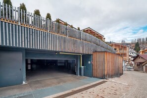 A building with a garage entrance, a ramp, and a wooden fence with greenery on top. - Apartment 'Casa Patty Moena' with Mountain View, Balcony and Wi-Fi (Moena)