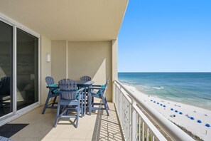 Een balkon met een tafel en stoelen, uitkijkend op een strand met parasols.