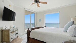 Een slaapkamer met een bed, een televisie, een plafondventilator, een dressoir en uitzicht op de oceaan.