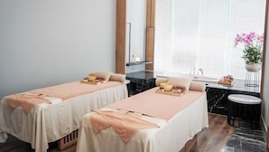Une salle de spa équipée de deux lits, d’un lavabo en marbre et d’une fenêtre avec des stores.
