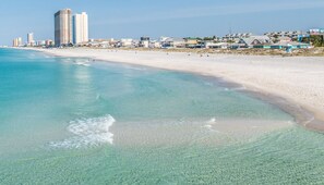 Una playa con agua turquesa cristalina, una orilla de arena y edificios al fondo.