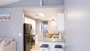 Eine moderne Küche mit Kochinsel, ein Essbereich mit Tisch und Stühlen sowie ein Wohnzimmer mit Sofa.