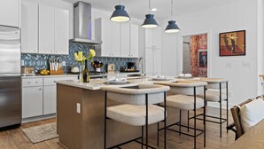 Une cuisine moderne avec des meubles blancs, un réfrigérateur en acier inoxydable et un îlot central doté de tabourets de bar.