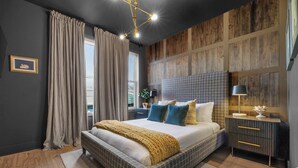 Une chambre avec un grand lit, une table de chevet, une lampe et une vue sur l’extérieur.