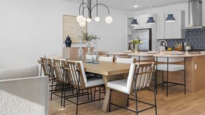 Une cuisine moderne avec une table à manger en bois, des tabourets de bar, des luminaires suspendus et un îlot de cuisine.
