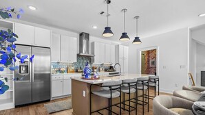 A modern kitchen with white cabinets, a stainless steel refrigerator, and a central island with bar stools. - Nash Skyline Views Rooftop with Fire Pit  Grill (Nashville)
