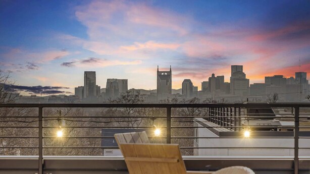 A rooftop terrace with a city skyline view, a wooden chair, and a table. - Nash Skyline Views Rooftop with Fire Pit  Grill (Nashville)