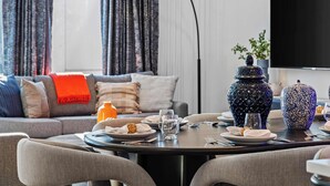 A dining area with a round table set for two, a sofa with cushions, a TV, and decorative vases. - Nash Skyline Views Rooftop with Fire Pit  Grill (Nashville)
