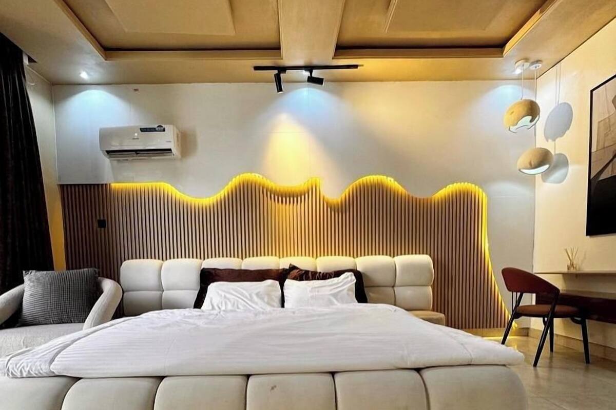 A modern bedroom with a large bed, a built-in headboard, a wall-mounted air conditioner, and a unique wavy wall design.