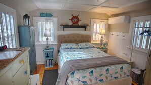 Une chambre à coucher comprenant un lit, une commode, une étagère avec des objets décoratifs, une horloge murale et une enseigne sur laquelle on peut lire « CAPE COD ».