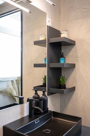 A modern bathroom with a black sink, a mirror, and two shelves with candles and a bottle. - Aram`s Luxury Port House (Kos)