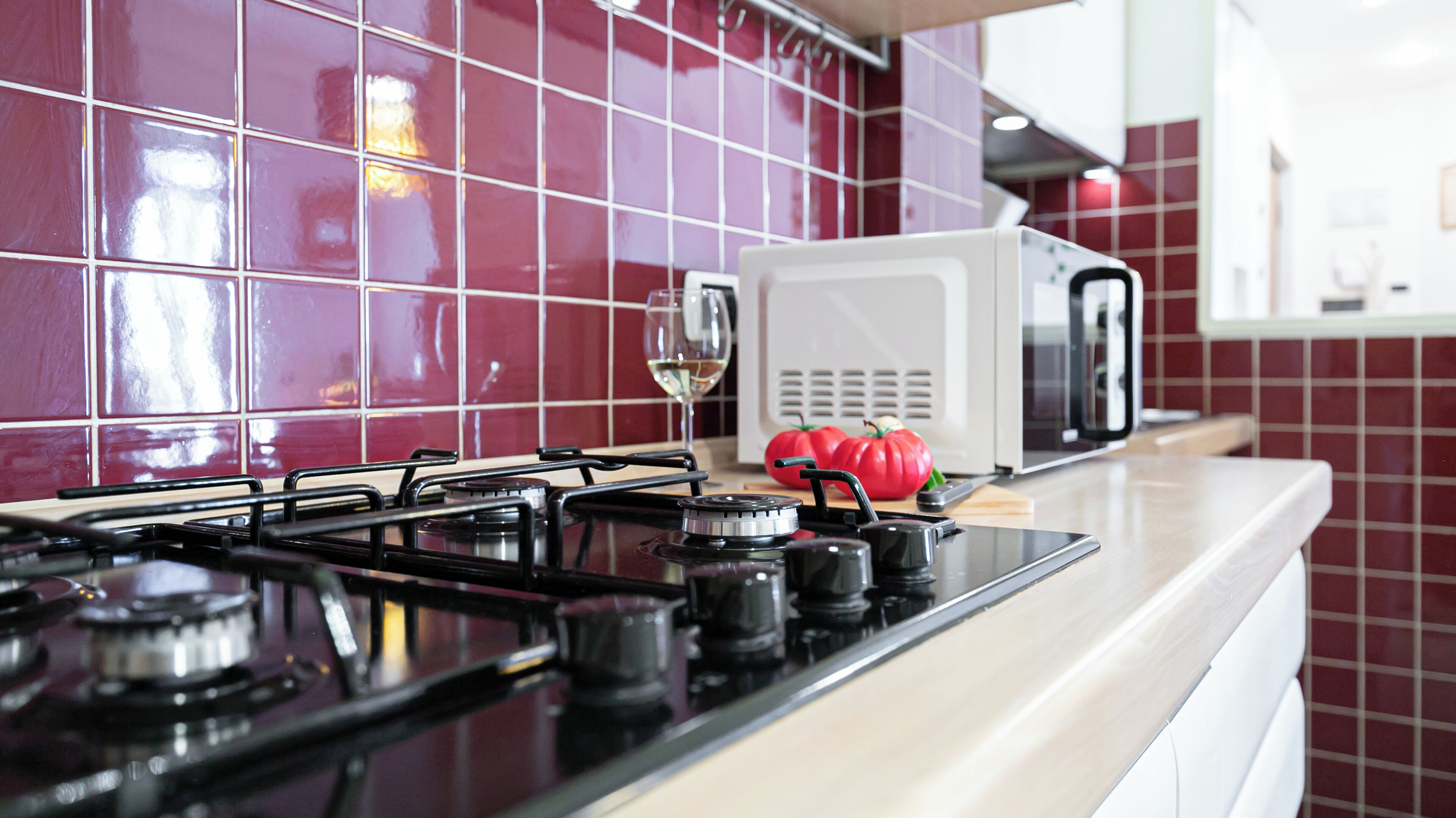 A kitchen with a gas stove, a microwave, and a red tomato on the counter.