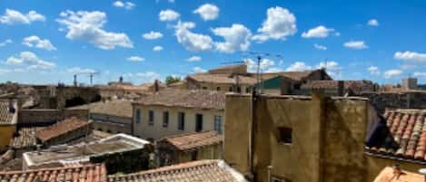 A view of a cityscape with terracotta-tiled rooftops, buildings with varying heights, and a clear blue sky with scattered clouds.