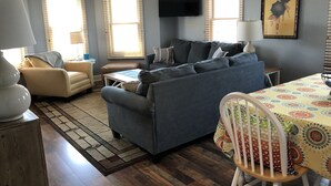 Ein Wohnzimmer mit einer Couch, Sesseln, einem Esstisch und einem an der Wand befestigten Fernseher.