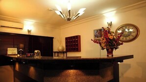 A reception area with a marble counter, a clock, a vase of flowers, and a framed certificate on the wall. - Lekki Suites (Lekki)