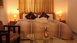 A hotel room with a bed, two nightstands, a chair, and a glass table with a bottle. - Lekki Suites (Lekki)