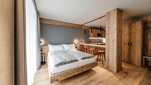 A modern bedroom with a loft-style bed, wooden flooring, and a kitchen area with stools. - El Giof Alpine Home (Pellizzano)