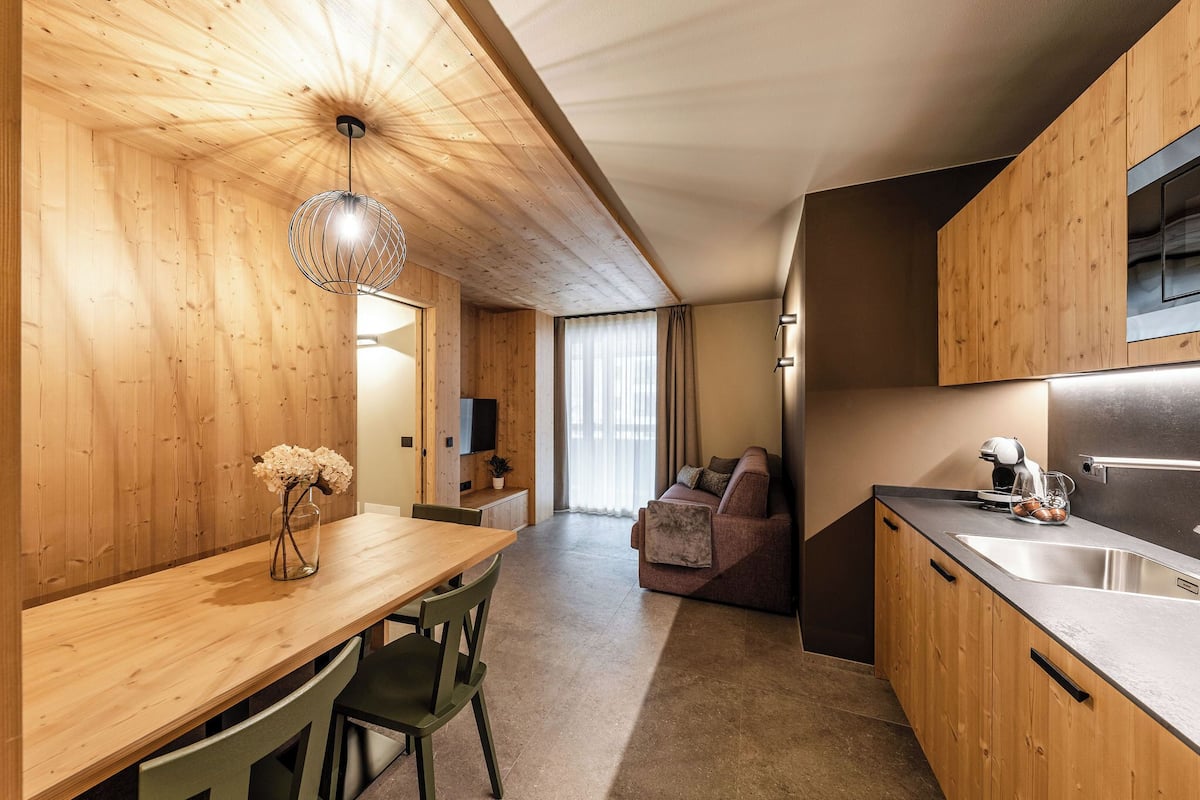 A modern kitchen with wooden cabinets, a dining area with a wooden table and chairs, and a living area with a sofa.