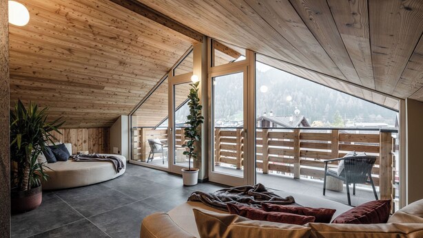 A spacious living area with a wooden ceiling, large windows, a sofa, and a potted plant. - El Giof Alpine Home (Pellizzano)