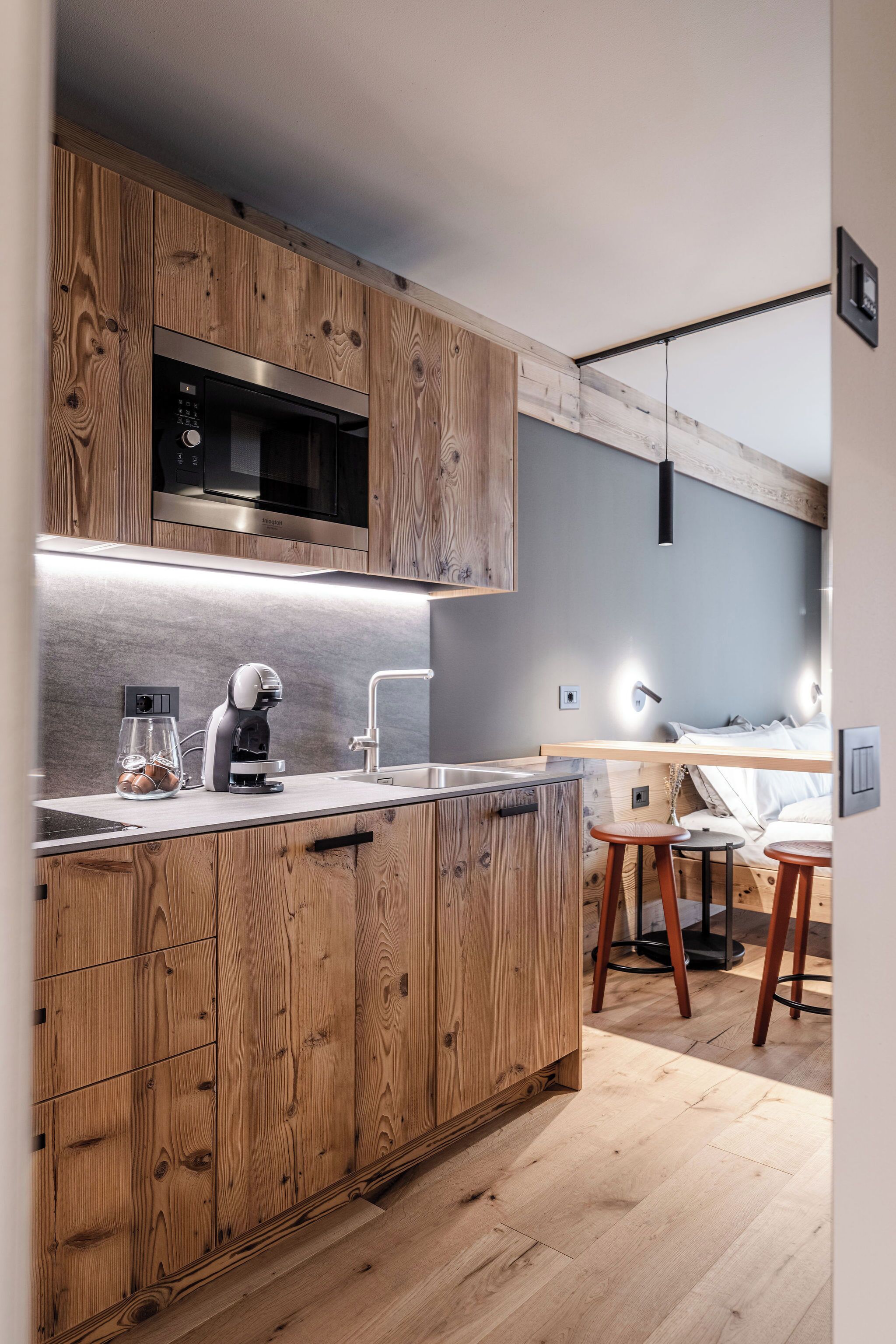 A modern kitchen with wooden cabinets, a built-in microwave, and a coffee machine.
