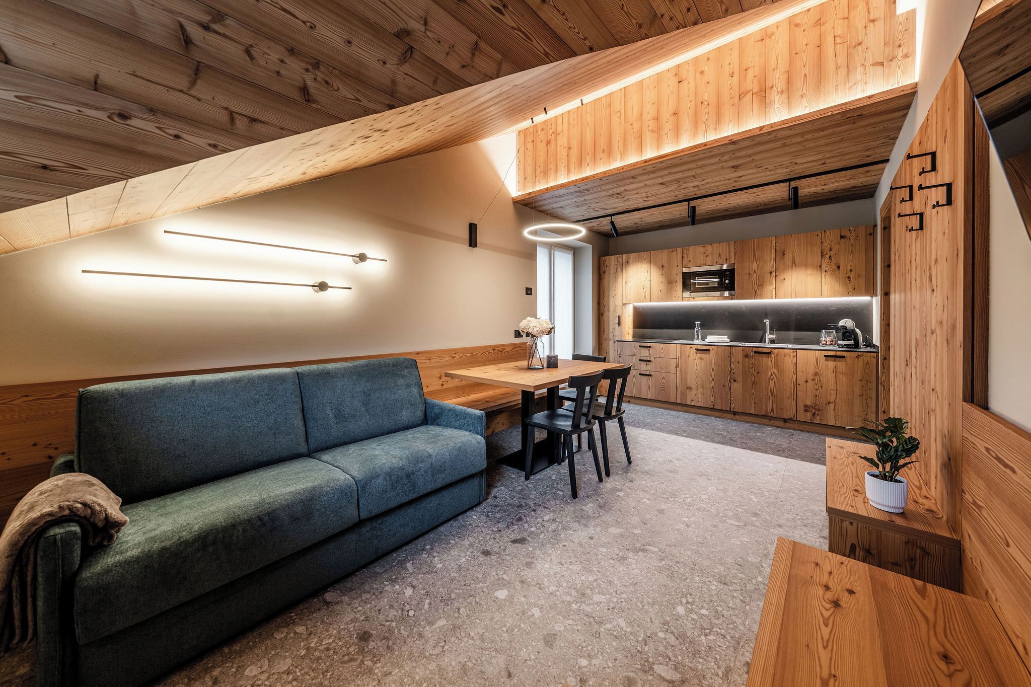 A modern kitchen with wooden cabinetry and a dining area with a blue sofa and a wooden table.