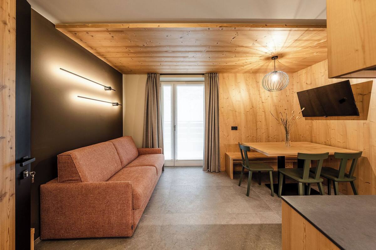 A modern interior with a wooden ceiling, a sofa, a dining table with chairs, and a large window with curtains.