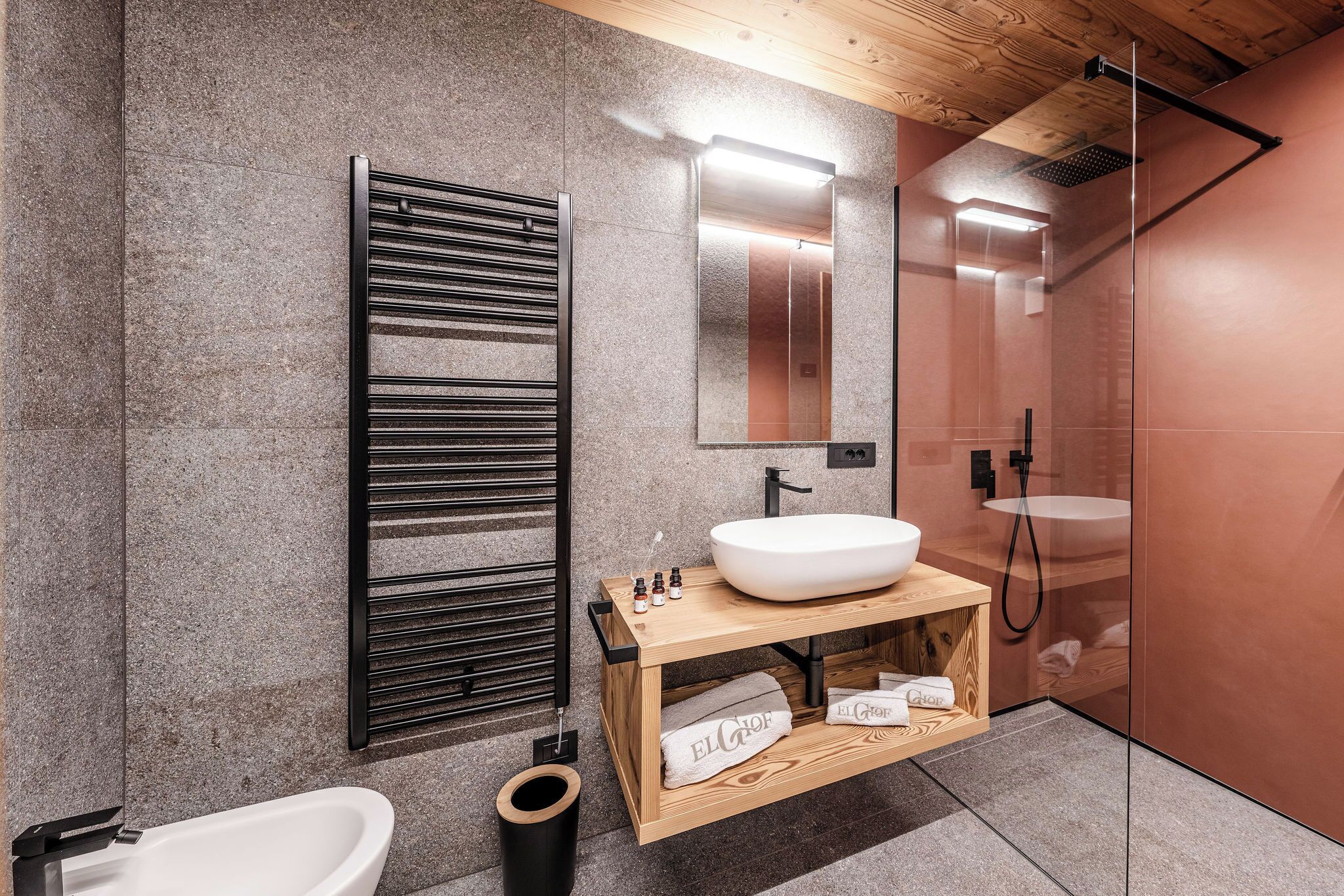 Een moderne badkamer met een vrijstaand bad, een houten wastafelmeubel met een grote wastafel, een handdoekrek en een douchecabine met glazen wanden.