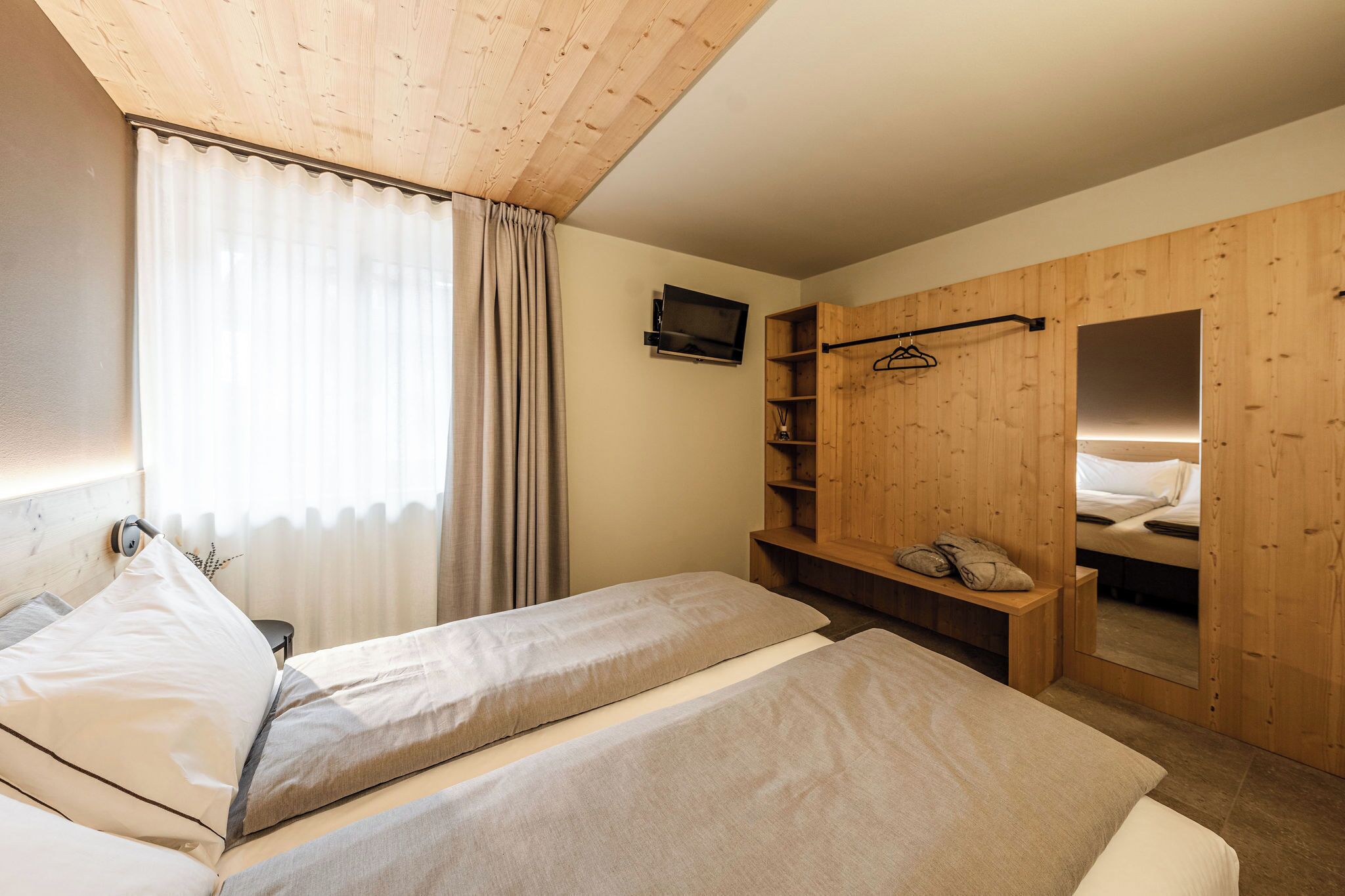 A room with two beds, a wooden wardrobe, a TV, and a mirror.