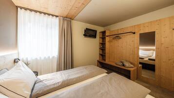 A room with two beds, a wooden wardrobe, a TV, and a mirror.