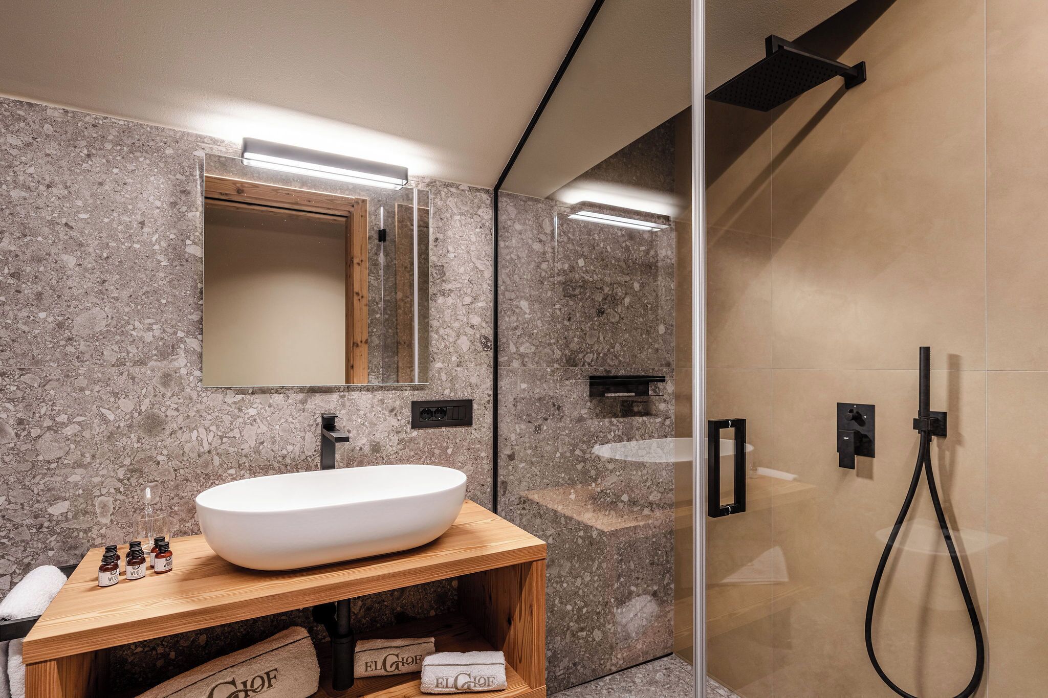 Ein modernes Badezimmer mit einem großen weißen Waschbecken, einem Holz-Waschtisch, einem Spiegel und einer Duschkabine.