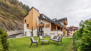 A modern building with a wooden facade, a balcony, and a well-maintained lawn with outdoor furniture. - El Giof Alpine Home (Pellizzano)