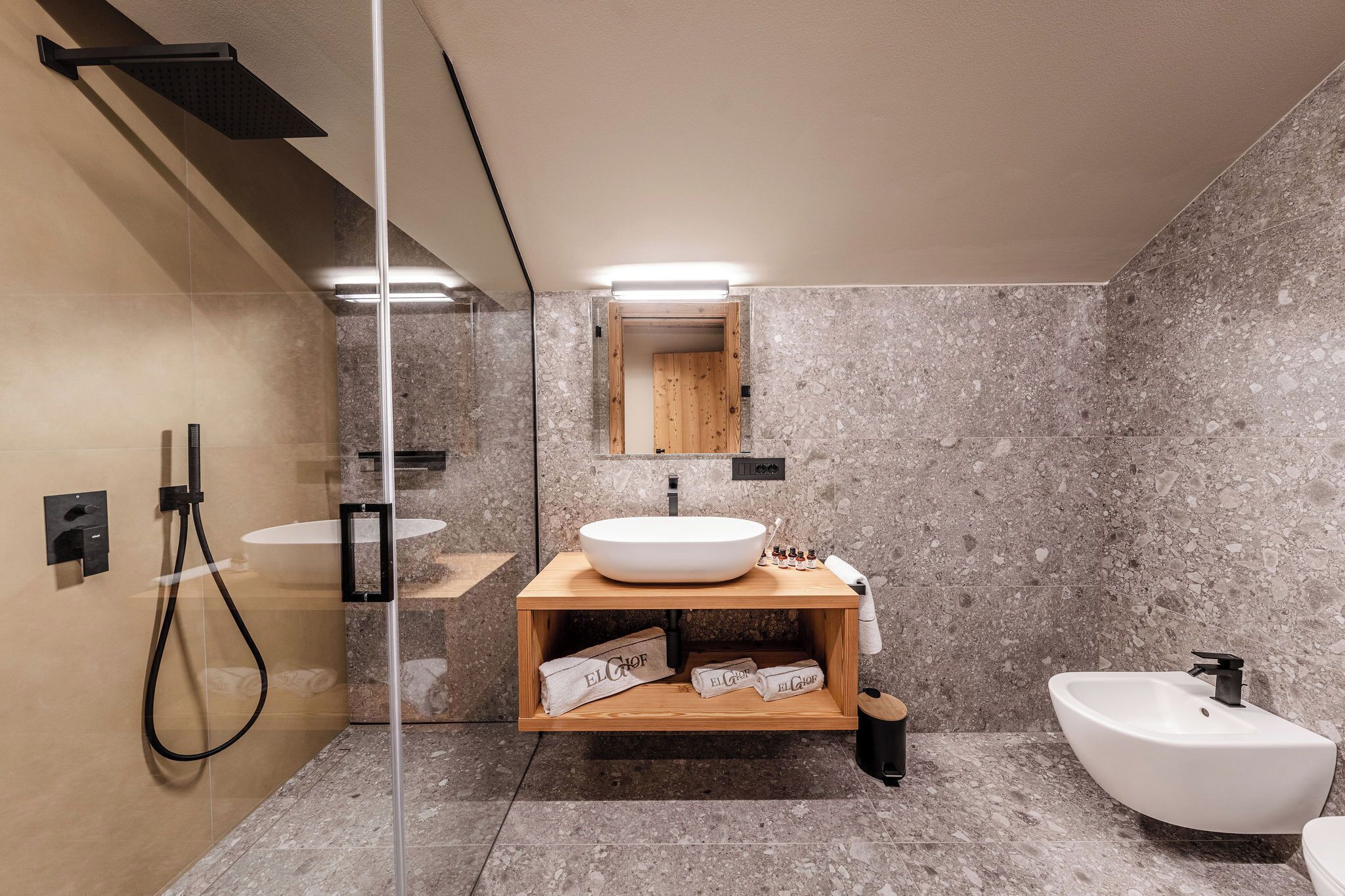 Een moderne badkamer met een grote spiegel, een houten wastafelmeubel, een losstaand wastafel en een bidet.